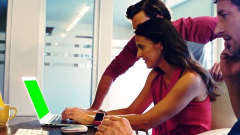 Male-graphic-designer-talking-on-mobile-phone-while-coworkers-using-laptop