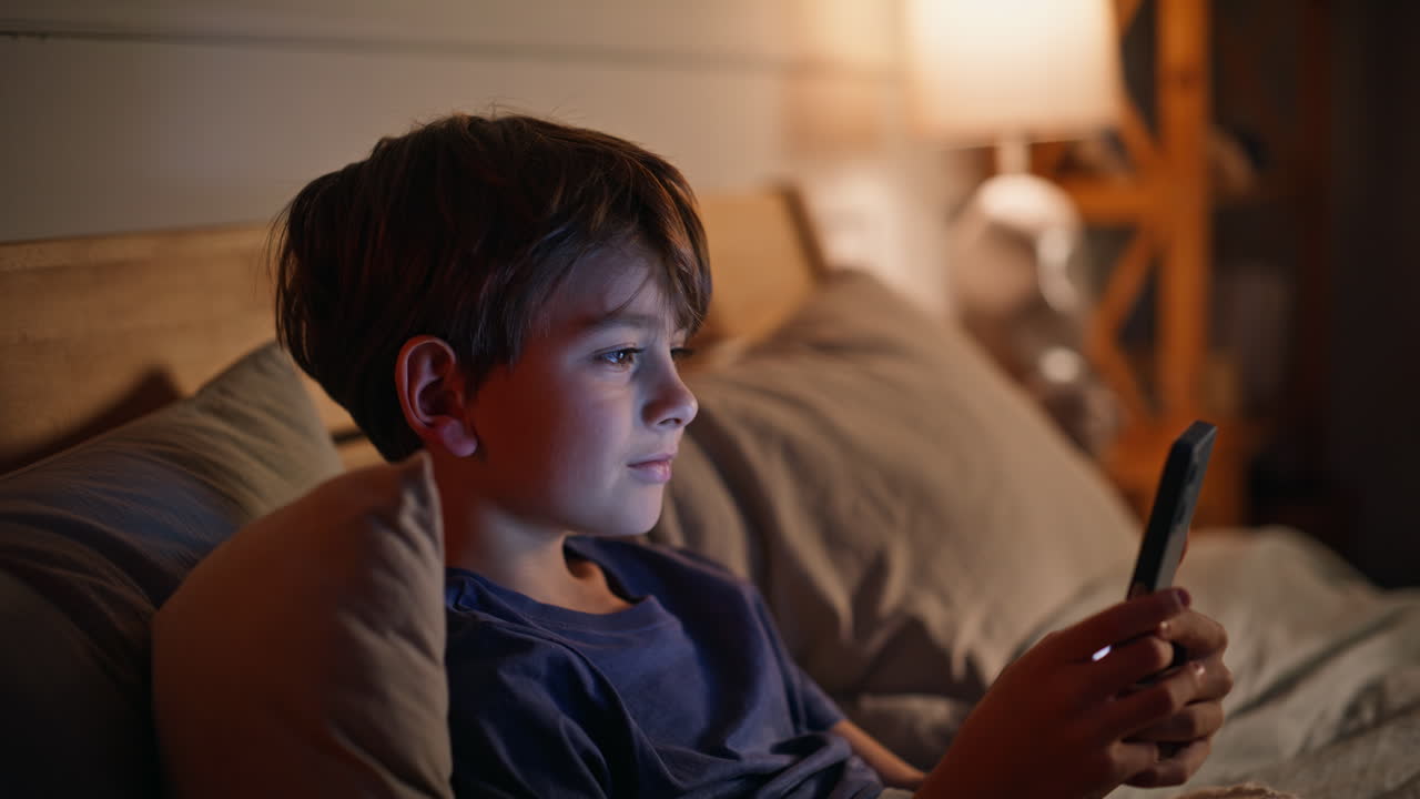 Child immersed smartphone content night lying bed closeup. Boy watching screen