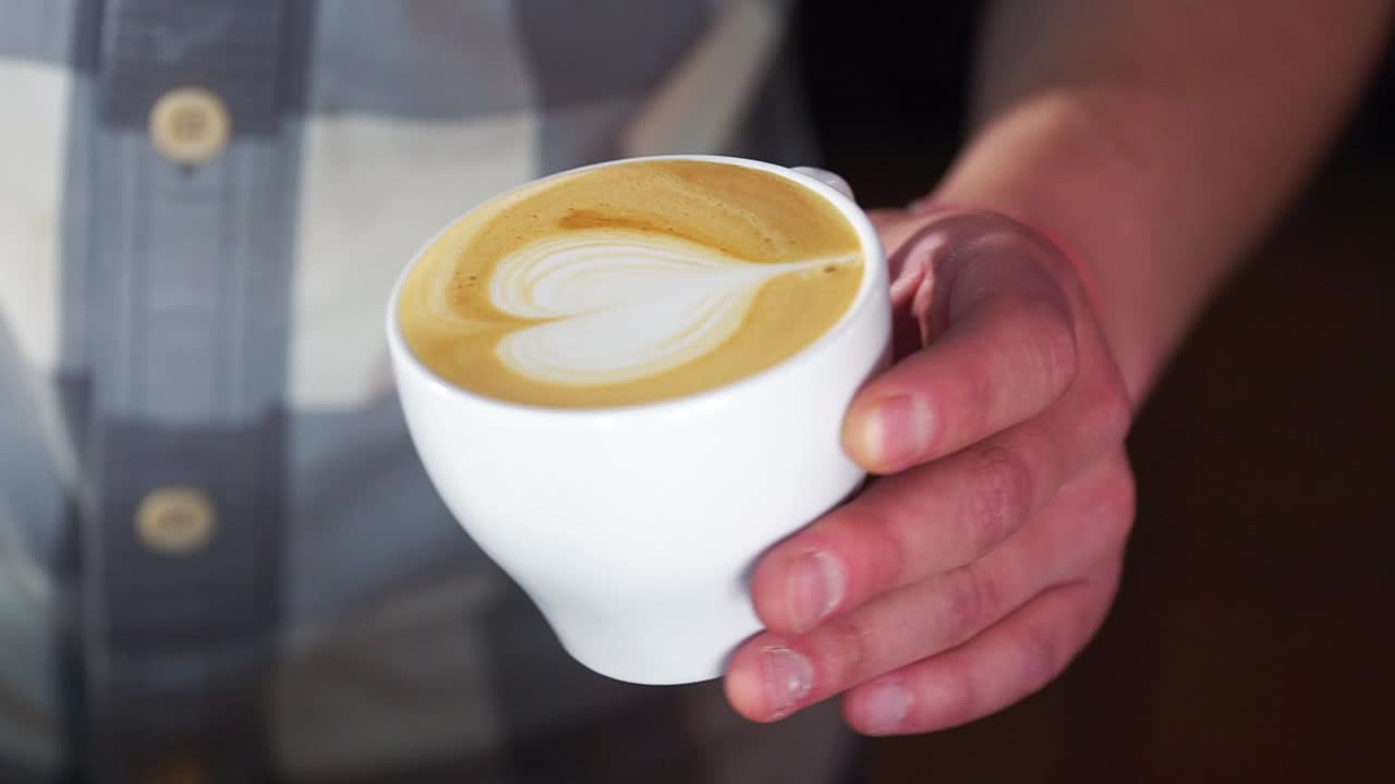 Barista pouring latte foam over coffee making a perfect cappuccino and creating a white heart. White cup with cappuccino
