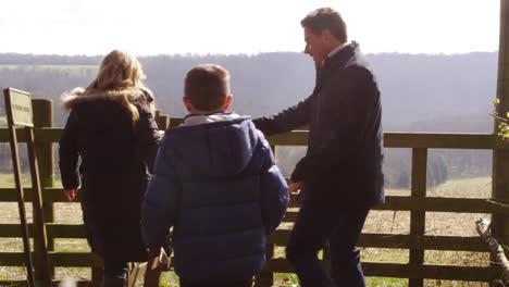 Familia-Con-Perro-Caminando-Por-La-Puerta-Rural,-Vista-Posterior,-Filmada-En-R3d