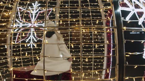 caucasian woman in white jacket dancing inside christmas decoration of lights