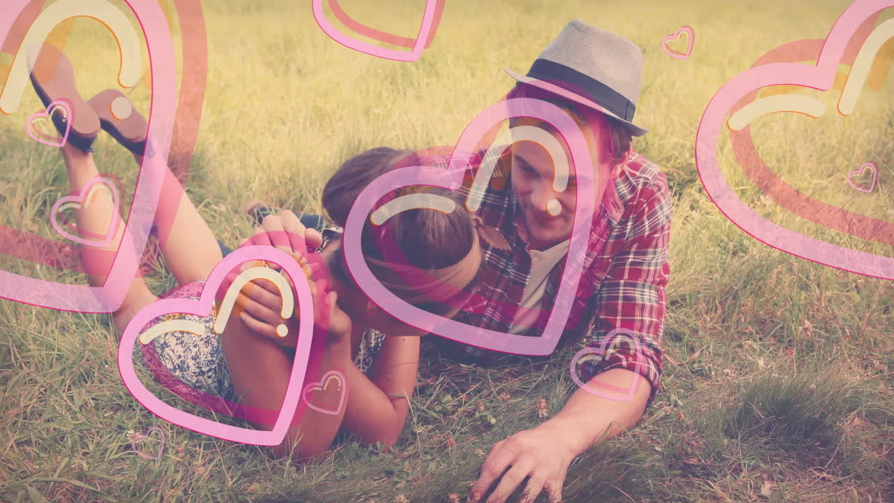 Young couple playfully lying on grass with heart animations surrounding them