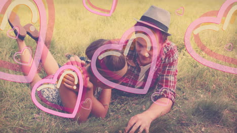 young couple playfully lying on grass with heart animations surrounding them