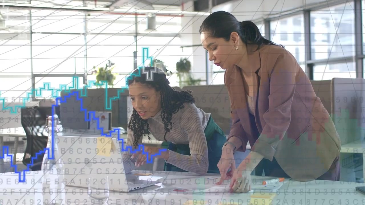 Duas mulheres no laptop digitando e apontando, projetando gráficos de negócios para revisão, com um colega se juntando.