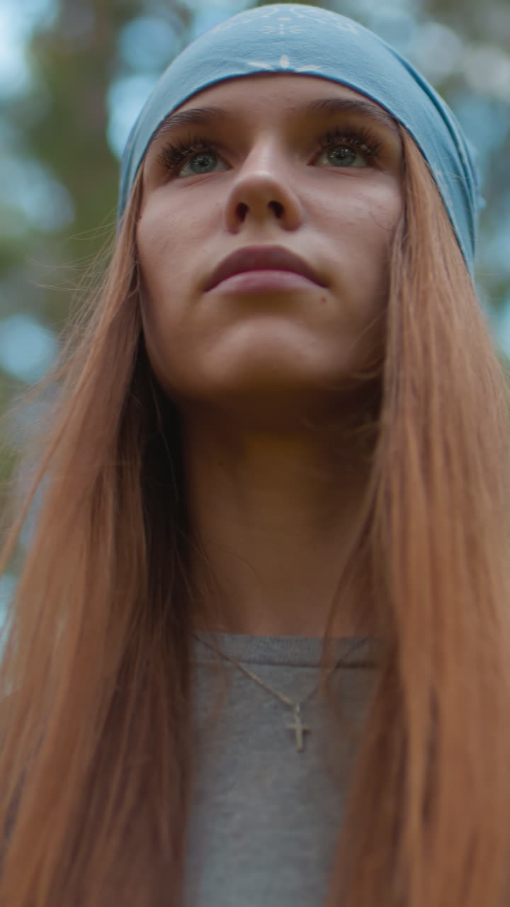 dama caminando a través de un bosque exuberante, mira a su alrededor contemplativamente, con bandana azul y mochila, rodeada de vegetación vibrante y árboles altos, con un brillo suave y natural en el fondo
