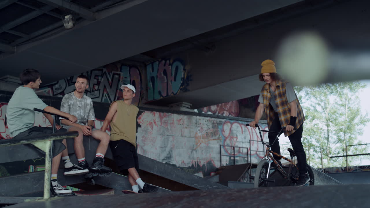 adolescentes activos viendo entrenamiento en bicicleta bmx en el parque de skate con graffiti.