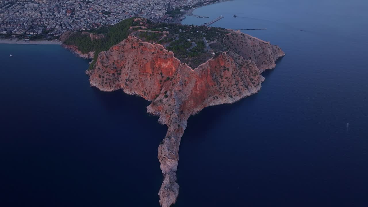Castello di Alanya al crepuscolo sopra il mare con una barca che naviga sotto