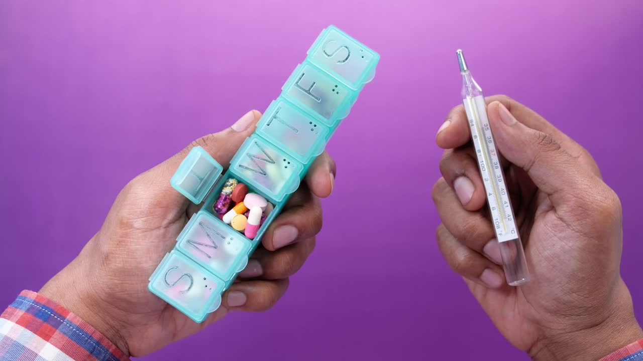 persona que sostiene el organizador de pastillas y el termómetro