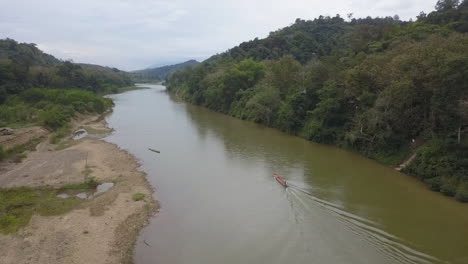 Low-aerial-follows-river-boat-motoring-up-Mekong-River-in-rural-Laos