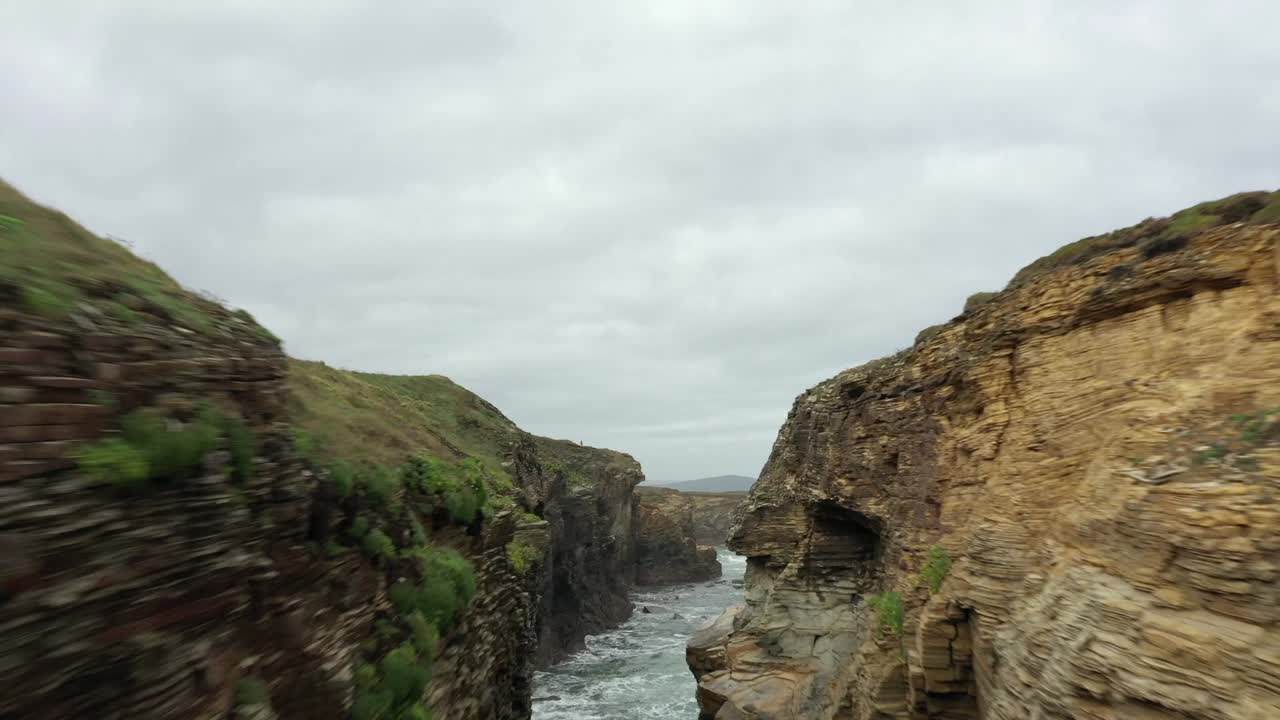 Risky drone flight between rocky walls at Las Catedrales beach. Aerial forward