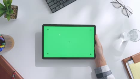 vista de arriba hacia abajo de una computadora portátil con pantalla verde simulada pantalla chromakey en un escritorio de oficina de madera al lado de la libreta con bolígrafos, gafas y un vaso de agua.