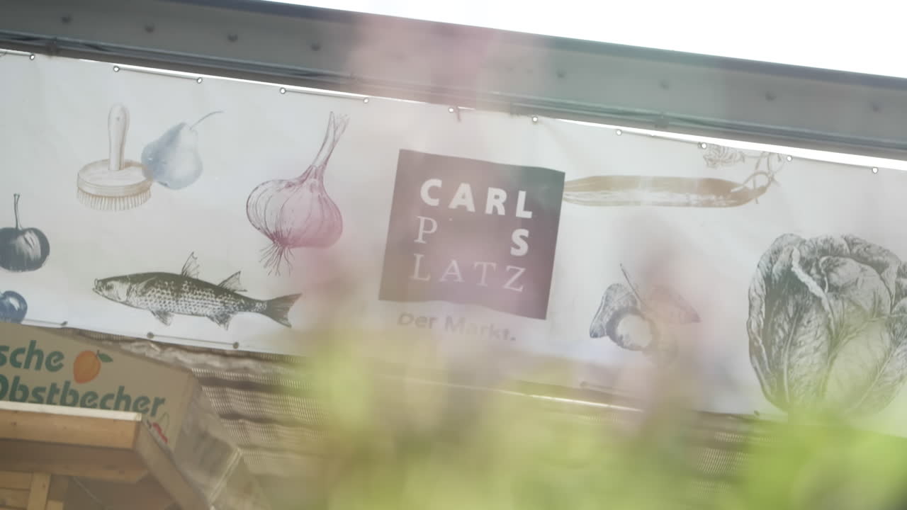 High-resolution video of the entrance of Carlsplatz in D&uuml;sseldorf, a prominent white banner hangs above the entrance, featuring painted images of a fish, garlic, salt, and a pear