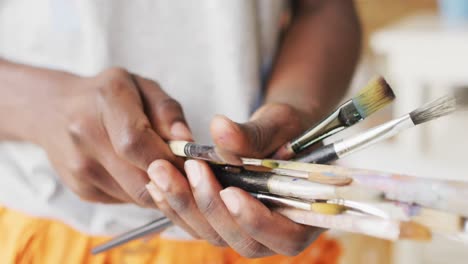sección media de un pintor afroamericano que sostiene pinceles en el estudio del artista