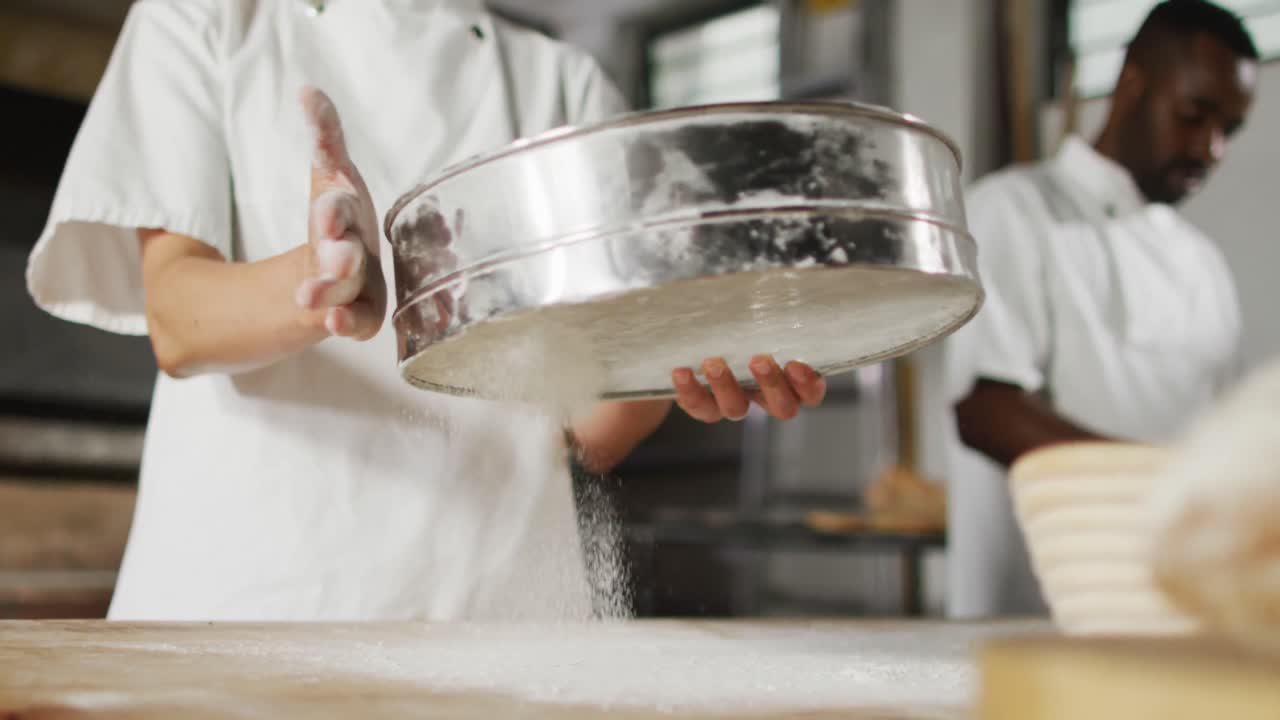 Animation of midsection of asian female baker sieving flour on board