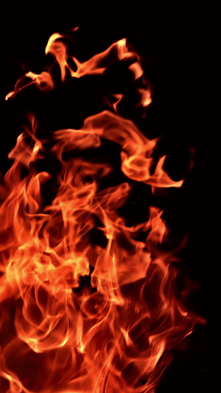Fiamme di fuoco impetuose che danzano nell'oscurità. Fiamma arancione che sale e si estende verso l'alto. Primo piano. Video verticale