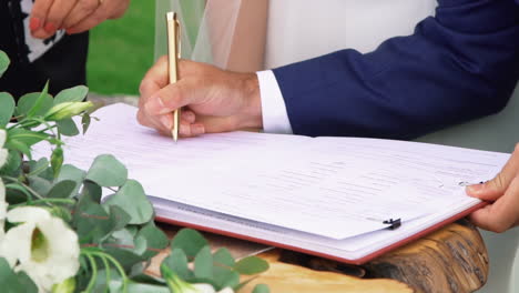 novio con traje azul firmando un certificado de matrimonio con un bolígrafo dorado