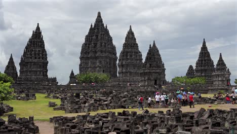 indonesia, prambanan temple on a cloudy day from a distance, camera tilts up and covering all temples, people walking around the temple complex.