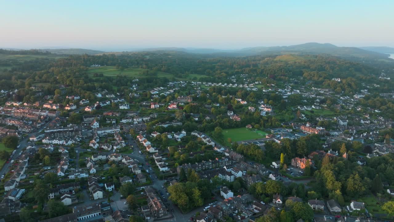 Rural urban town amongst woodland and hills at sunrise. Lateral camera movement. Summer. Windermere, Cumbria, UK