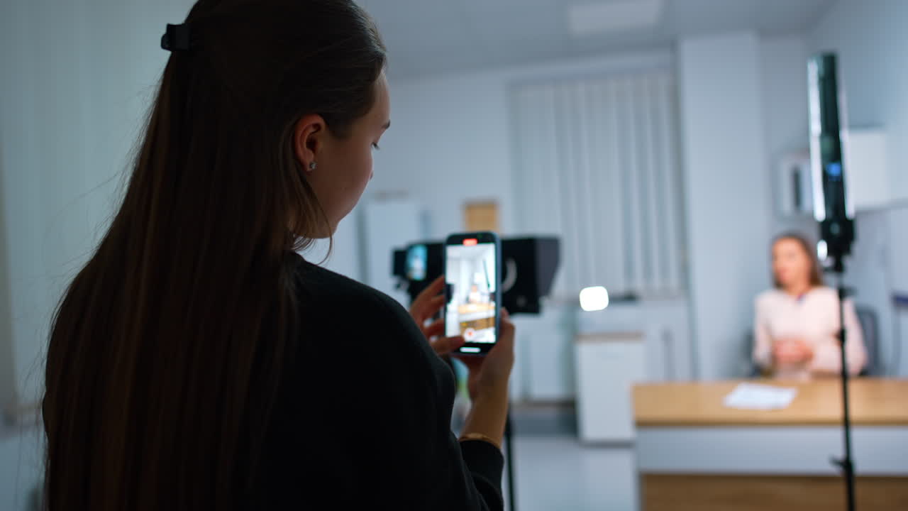 Young woman stands holding her phone and recording video. Recording a content for internet blog. Blurred backdrop.