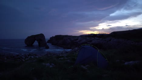 remote wild camping tent near unique rock formation ocean cliff waves