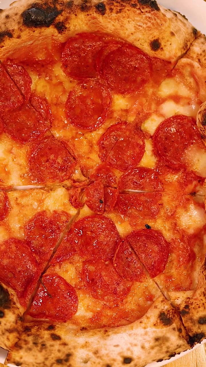 Inquadratura dall'alto di mani che tagliano una pizza al lievito madre e salame piccante su un tavolo di legno di un ristorante.