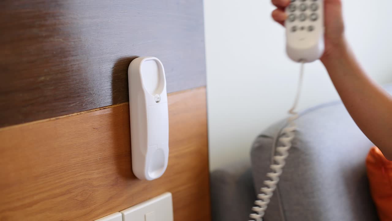 한 사람이 편안한 방에서 벽에 장착된 전화를 들고 가정 기술과 간단한 상호 작용을 보여줍니다.