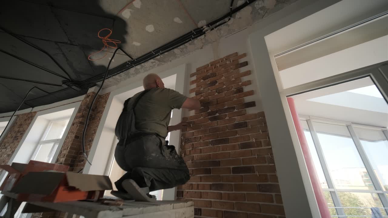Specialist installing decorative brick tiles on the wall. Renovation in the loft style. Construction works