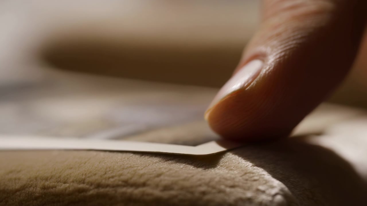 Ekstremt nærbillede af en højre fingerspids, der presser et klæbende plaster på tekstureret hud, hvor plasterets kant løber horisontalt hen over den nederste tredjedel, mens fingerspidsen.
