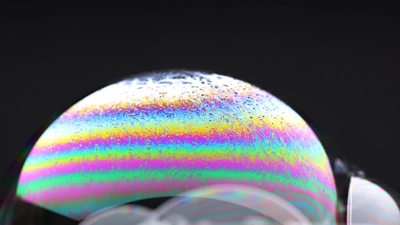 Vibrant soap bubbles display shifting rainbow colors against a dark background, highlighting dynamic reflections and fluid motion