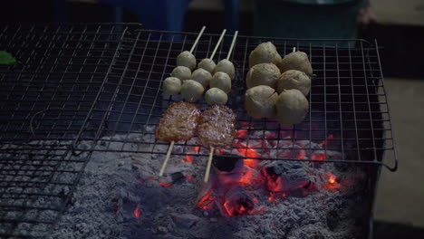 primer plano de la preparación de cerdo asado a la parrilla en brochetas de madera usando calor de carbón