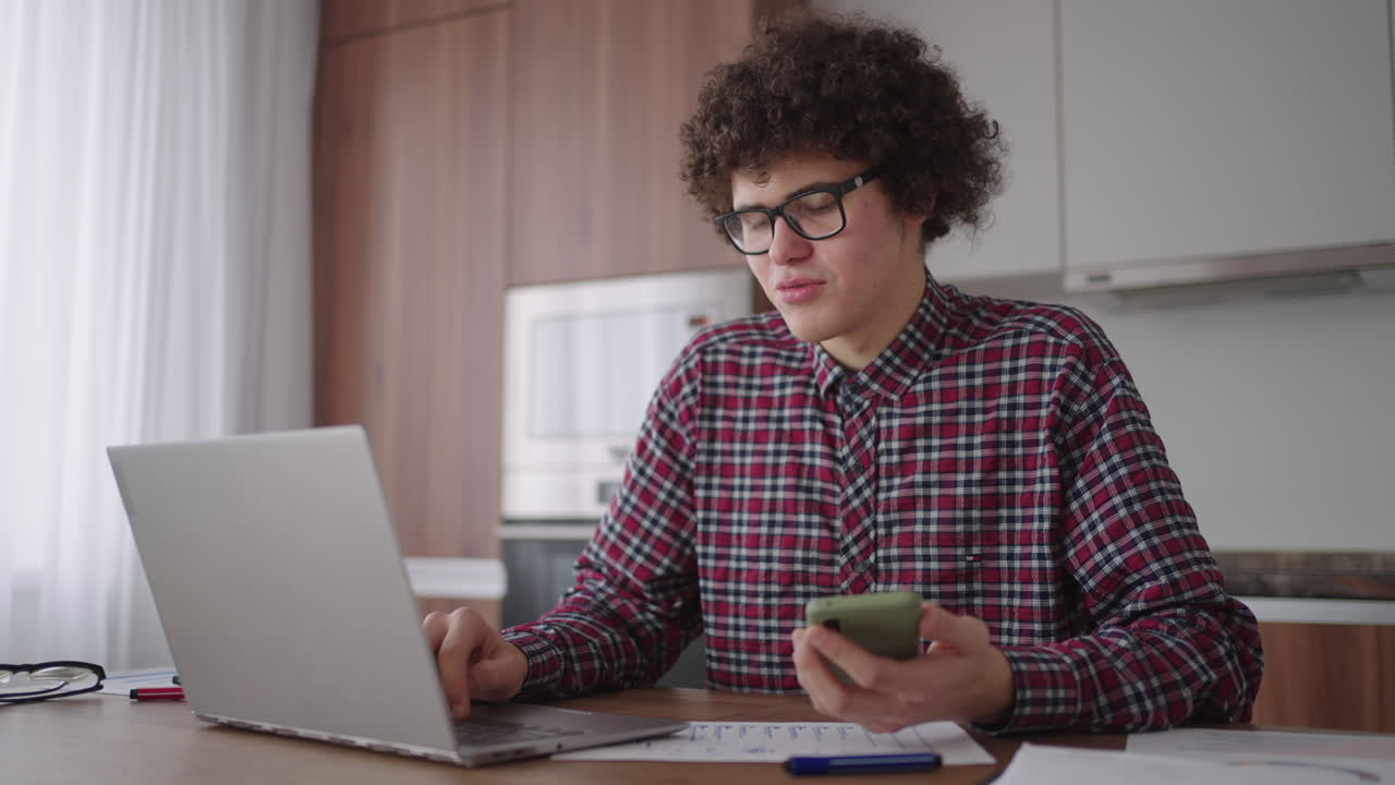 Young man with smartphone in his hands. Modern businessman or student at home office. Freelancer at work. Young student man study at home with laptop and uses a smartphone