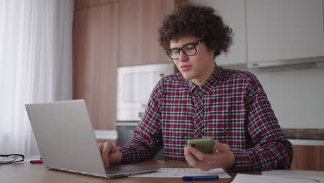 young man with smartphone in his hands. modern businessman or student at home office. freelancer at work. young student man study at home with laptop and uses a smartphone