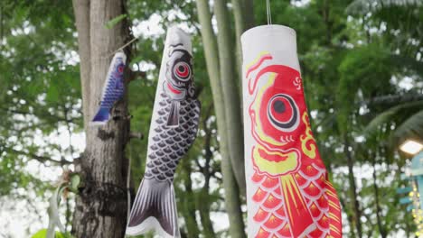 colorful koinobori carp-shaped windsocks fluttering among trees, shallow depth of field