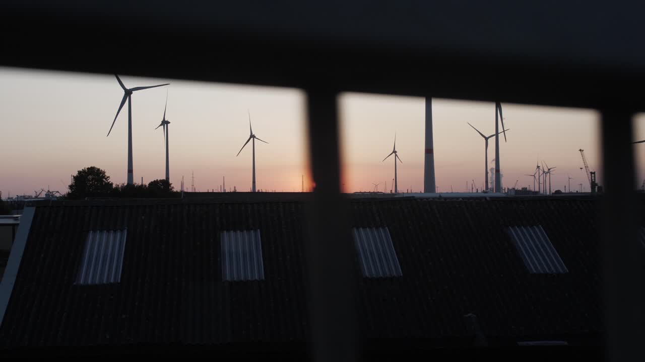 Cinematic slow motion shot behind a railing, view of the sunset with wind turbines in the background