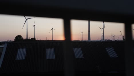 Toma-Cinematográfica-En-Cámara-Lenta-Detrás-De-Una-Baranda,-Vista-De-La-Puesta-De-Sol-Con-Turbinas-De-Viento-En-El-Fondo