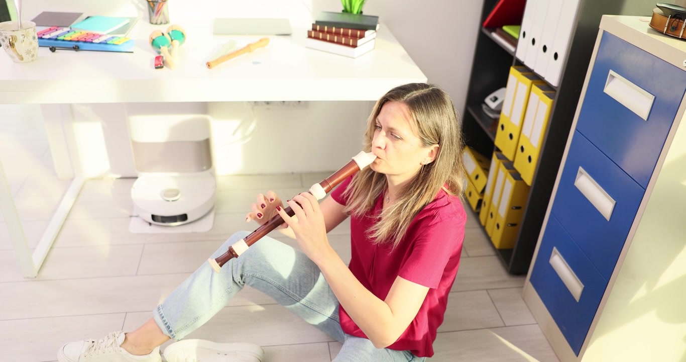 Donna seduta sul pavimento concentrata a suonare un flauto di legno marrone.
