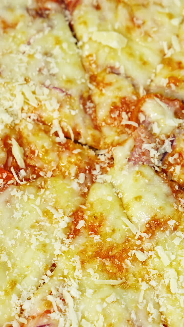 Ready pizza is sprinkling with cheese. Well baked pizza with melted cheese and other ingredients. Tasty snack. Close-up. Top view. Vertical video