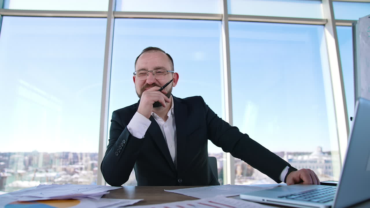 Portrait of a bearded businessman at workplace. Entrepreneur in glasses sitting at desk and thinking about his business.