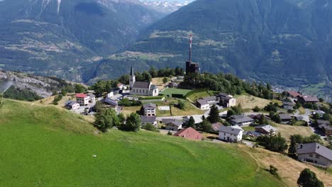 Wunderschönes-Bergdorf-Feschel-Guttet-Mit-Einer-Schönen-Kirche-Und-Einer-Großen-Fernsehantenne-In-Einer-üppig-Grünen-Landschaft,-Schweizer-Berge-Im-Hintergrund