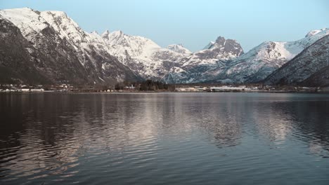 stunning shot taken across a still lake, with huge snow-covered mountains surrounding the lake