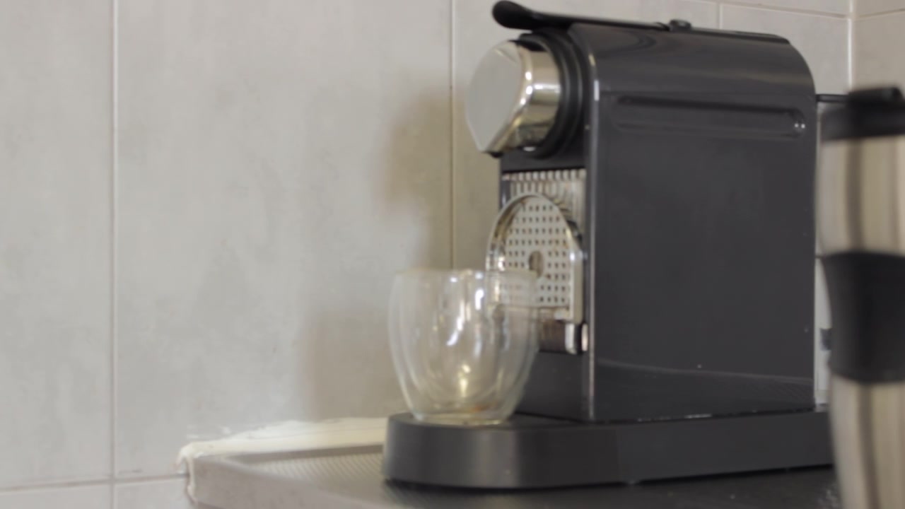 Bir espresso kahve makinesinin altındaki boş şeffaf bir bardağı gösteren kaydırma çekimi. Bir damla kahve bardağa düşüyor.