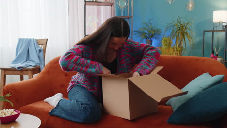 Happy-young-woman-shopper-unpacking-cardboard-box-delivery-parcel-online-shopping-purchase-at-home