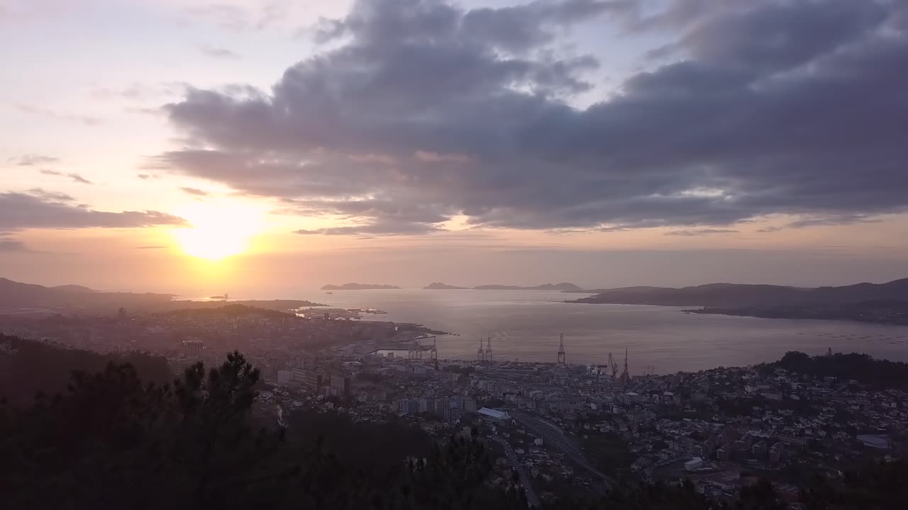 Aerial view of the coast city of Vigo in the atlantic ocean at sunset with the natural park of the Cies island in the background. Drone stablishing shot forward travelling