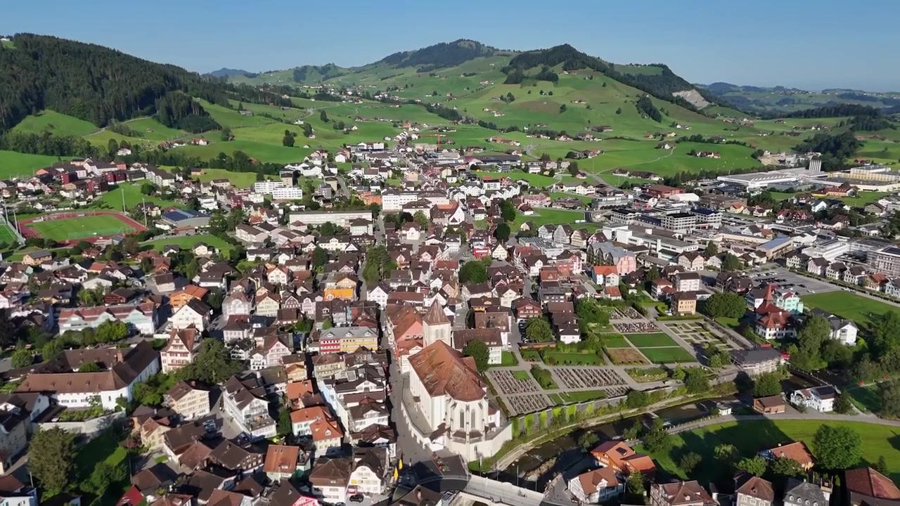 Volo di drone sopra la storica città svizzera di Appenzell con antichi edifici e una chiesa in estate. Montagne verdi e rigogliose contro un cielo blu. Ampia ripresa a volo d'uccello.