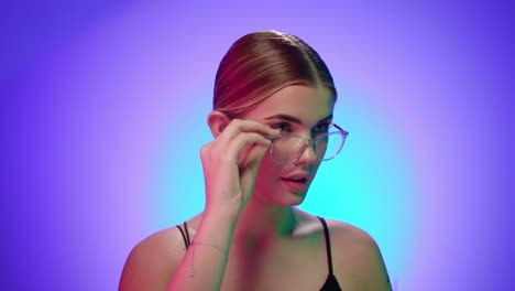 joven rubia caucásica mira por encima de sus gafas asombrada y luego se ríe, retrato filmado en el estudio