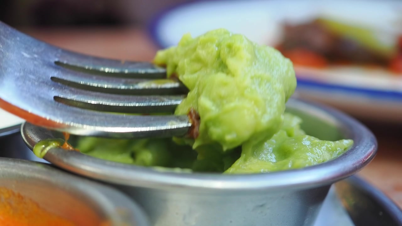 Forchetta che raccoglie guacamole fresco da una ciotola di metallo