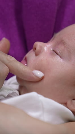 beautiful infant in mother's embraces sleeps sweetly. mother is trying to wake her son up by touching his chin, nose, cheeks. cute boy doesn't want to wake up. vertical video