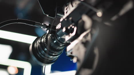 close up camera lens focus ring and attached cables reflecting blue and white neon studio lights, highlighting mechanical textures and precise manual adjustments for broadcast filming setup