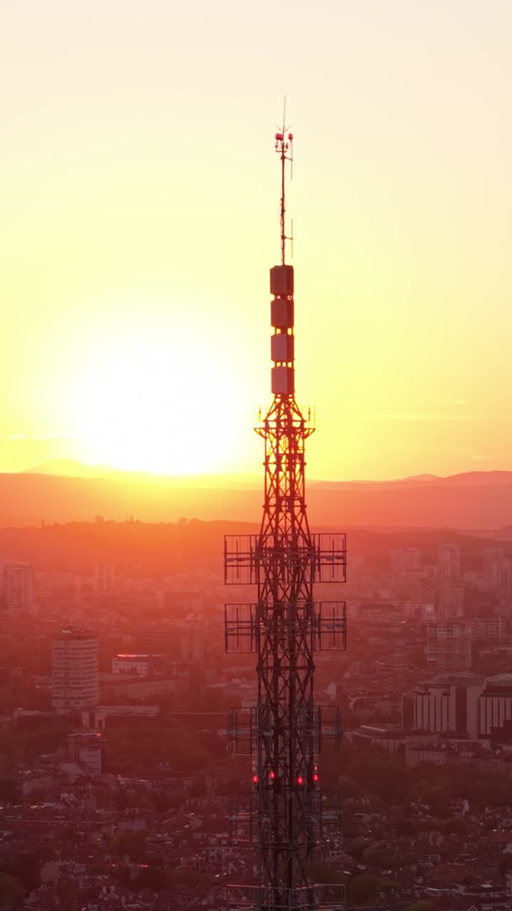 Cinematic vertical drone shot of Sofia, Bulgaria, during a stunning sunset. The TV Tower dominates the city skyline as warm hues fill the sky.