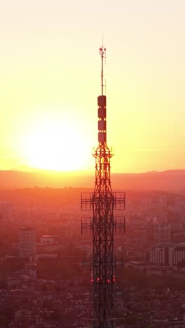 cinematic vertical drone shot of sofia, bulgaria, during a stunning sunset. the tv tower dominates the city skyline as warm hues fill the sky.